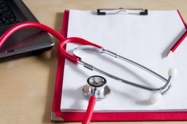 Kırmızı bir steteskop ve kırmızı bir kağıt üzerinde kırmızı bir kalem. Dizüstü bilgisayarın yanında. 