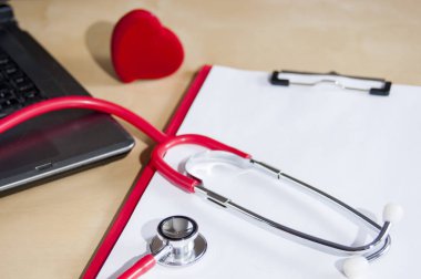 Kırmızı stetoskop, kırmızı panoda tonometre. Dizüstü bilgisayarın ve kalbin yakınında.