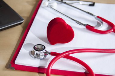 Kırmızı bir panoda kırmızı stetoskop ve kalp. Dizüstü bilgisayarın yanında. Tıbbi cihazlar.