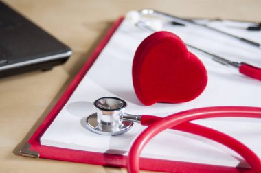 Kırmızı bir panoda kırmızı stetoskop ve kalp. Dizüstü bilgisayarın yanında. Tıbbi cihazlar. Tedavi, sağlık.