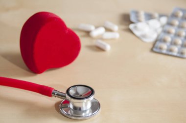 Kırmızı stetoskop ve kırmızı kalp masada. Tabletlerin ve kapsüllerin yakınında