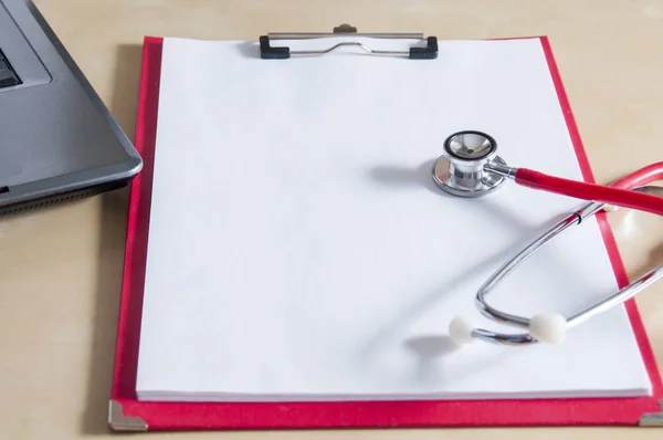 Red stethoscope on a red clipboard. Near laptop. Medical device.