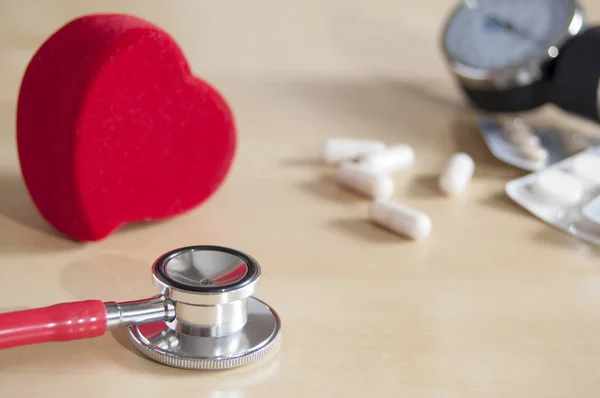 Estetoscopio rojo y corazón rojo en una mesa. Cerca de tabletas, cápsulas y tonómetro. Dispositivo médico . —  Fotos de Stock