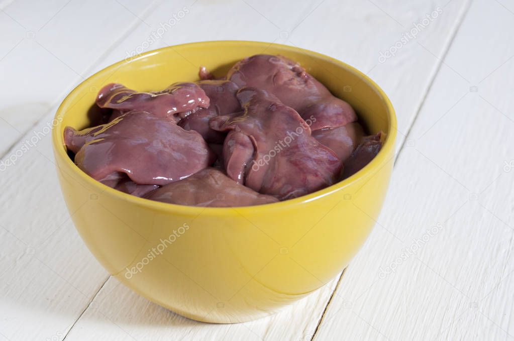 Raw chicken livers in a yellow bowl on a white wooden table. Clo