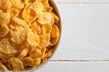 Beyaz ahşap bir masanın üzerinde mısır gevreği olan beyaz kase. Çerçevenin sol tarafını işgal eder.