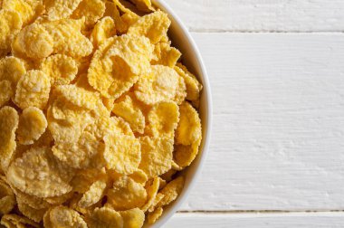 Beyaz ahşap bir masanın üzerinde mısır gevreği olan beyaz kase. Çerçevenin sol tarafını işgal ediyor. Yatay çerçeve.