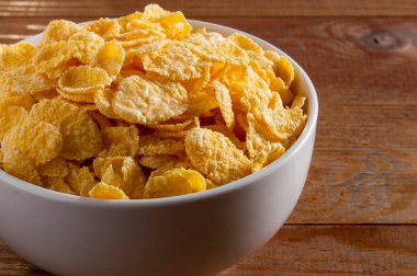 Kahverengi ahşap bir masanın üzerinde mısır gevreği olan beyaz kase. Yatay çerçeve.