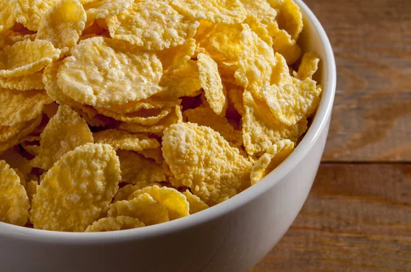 Kahverengi ahşap bir masanın üzerinde mısır gevreği olan beyaz kase. Topu çerçevenin sol tarafına at. Yatay çerçeve.