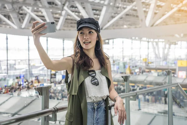 Backpacker gezginler Asyalı kadınlar şapka giyen havaalanında uçak bağlama sırasında cep telefonları ile selfie vardır. Tatil ve seyahat konsepti