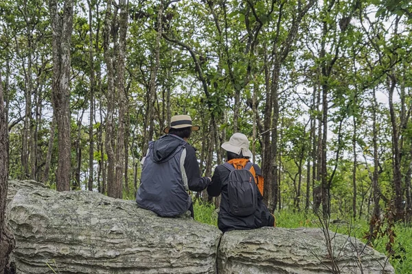 Two loving elderly friends have a relationship, wearing a cool jacket to relax and Sitting or talk on rocks in the mist in the forest.