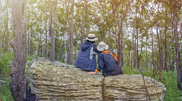 Two loving elderly friends have a relationship, wearing a cool jacket to relax and Sitting or talk on rocks in the mist in the forest.