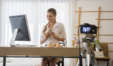  Ünlü blogger kavramı. Neşeli kadın blogger akıllı telefon ile video kayıt ve onun güzellik günlüğü için tavsiye verirken kozmetik ürünleri gösteriyor. Dijital kameralı cep telefonu odaklanın.
