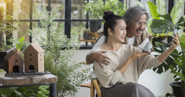 Пожилая пара, сидящая в зеленом доме, проводит конференцию со смартфоном, разговаривает с детьми
