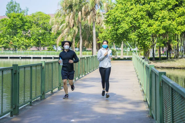 Asian couples wear masks that protect against covid 19 so happy and jogging together for health in the park.Social distancing and New normal concept.