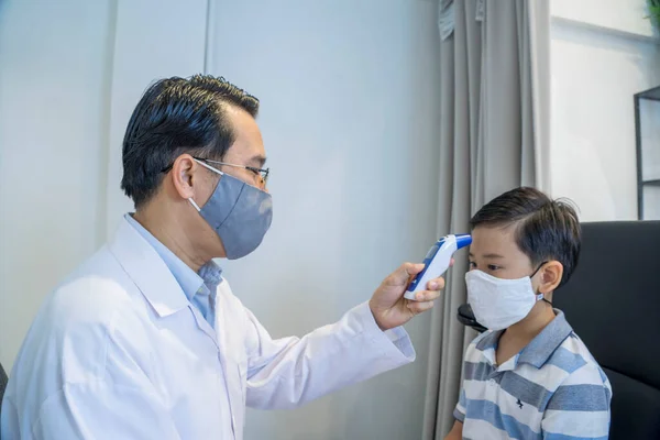 The eye doctor used an infrared thermometer to measure the boy\'s fever before examining his eyes in an optician.