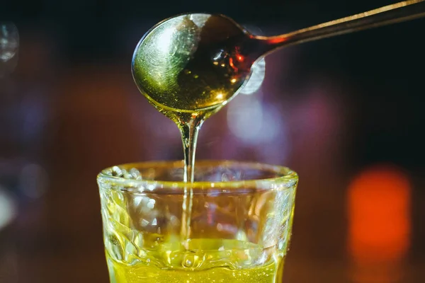liquid honey flows down a spoon into a glass