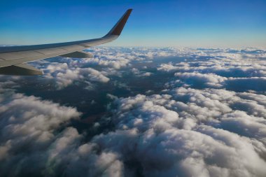 Bir uçağın kanadı mavi gökyüzüne ve bulutlara karşı kalkıyor.                           