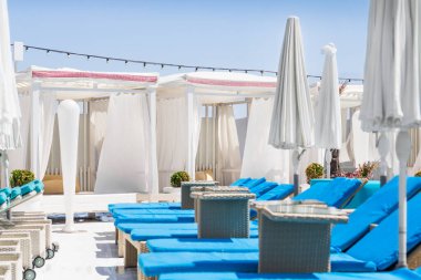 Deniz kenarındaki plaj kulübünde. Mavi şezlonglar, havuz kenarında şemsiyeler. Yaz mevsiminde deniz kıyısında.