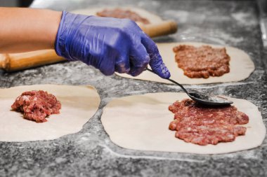 Mutfaktaki bir restoranda bir aşçı etli börek hazırlıyor. Eldivenli kadın elleri. Makro. Ev hanımı eti masaya sürer.