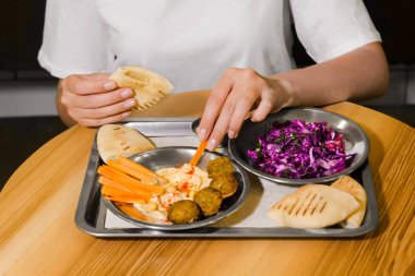 Kadın kafede humus ve pide ile falafel yiyor. Vejetaryen yemeği. Tabakta havuç ve lahana salatası. Glütensiz ve soyasız sağlıklı yiyecekler. Arap yemeği. İsrail ve Mısır 'ın ulusal yemeği