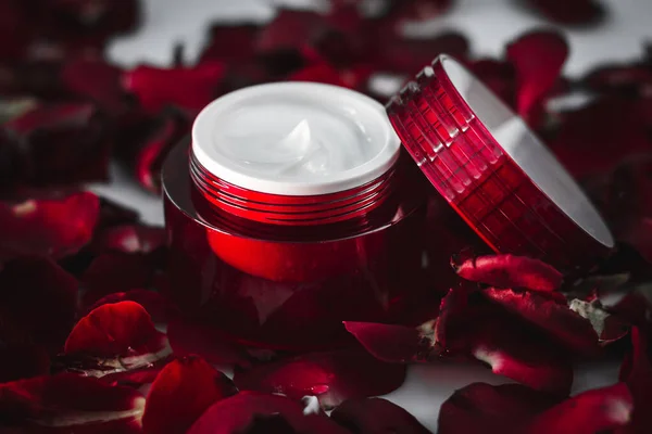 a moisturizing revitalizing cream for the face and around the eyes in a red jar against a background of scarlet rose petals. macro. cosmetics for women. care line of cosmetics for the face.