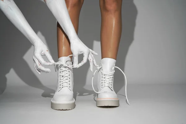 woman ties the laces on white shoes on a light background in the studio. close-up fashion footwear new collection autumn winter 21/22 fashion shooting