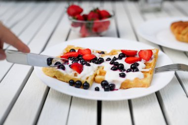 Adam waffle 'ları meyveli yoğurt ve çatal ve bıçaklı birinci şahıs görüşüyle kesiyor. Otelde kahvaltı.