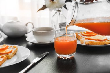 Beyaz cüppeli bir adam otel gözlemelerinde bir bardak portakal suyu kahvaltısı hazırlıyor. Meyveli waffle, kahve ve çay.