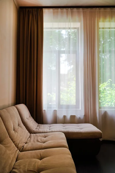 beige sofa in the corner of the room near the window. modern interior