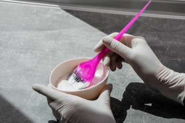 Beyaz lastik eldivenli kız elinde fırça tutuyor ve saç boyasını karıştırıyor. Saç maskesinde saç bakımı yapıyor.