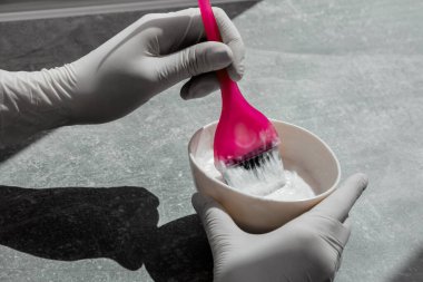 Beyaz lastik eldivenli kız elinde fırça tutuyor ve saç boyasını karıştırıyor. Saç maskesinde saç bakımı yapıyor.