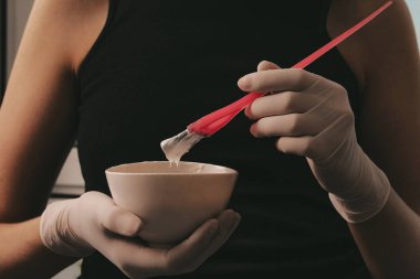 Beyaz lastik eldivenli kız elinde fırça tutuyor ve saç boyasını karıştırıyor. Saç maskesinde saç bakımı yapıyor.