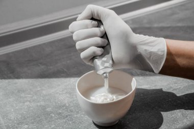 Beyaz koruyucu eldivenli bir kız saç boyasını oksitleyiciye sıkıştırıyor. İş yerindeki boyacı yakın plan saç bakım maskesinin saç boyası.