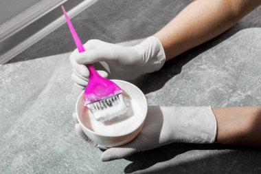 Beyaz lastik eldivenli kız elinde fırça tutuyor ve saç boyasını karıştırıyor. Saç maskesinde saç bakımı yapıyor.