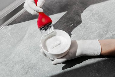 Beyaz kauçuk eldivenli kız elinde fırça tutuyor ve saç boyasını yakın plan saç bakımında karıştırıyor.