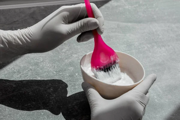 Beyaz lastik eldivenli kız elinde fırça tutuyor ve saç boyasını karıştırıyor. Saç maskesinde saç bakımı yapıyor.