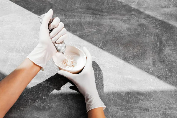 Beyaz koruyucu eldivenli bir kız saç boyasını oksitleyiciye sıkıştırıyor. İş yerindeki boyacı yakın plan saç bakım maskesinin saç boyası.