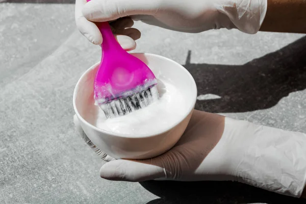 Beyaz kauçuk eldivenli kız elinde fırça tutuyor ve saç boyasını yakın plan saç bakımında karıştırıyor.