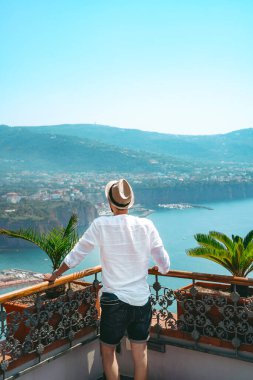 Beyaz gömlekli bir adam pozitano 'da bir villada dinleniyor ve terastan denize bakıyor.