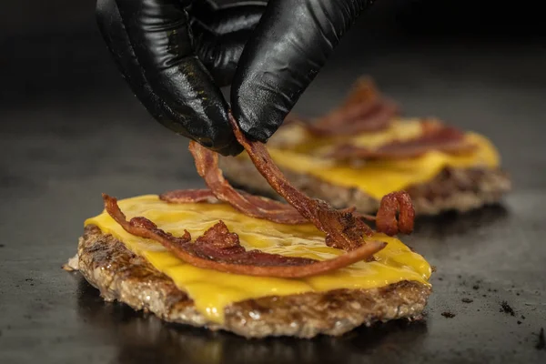 chef withg love putting bacon on hamburger