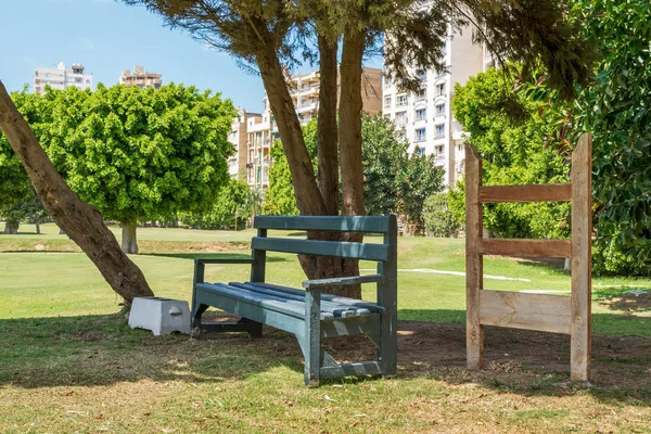 Banco de madera bajo el árbol en el parque de la ciudad — Foto de Stock
