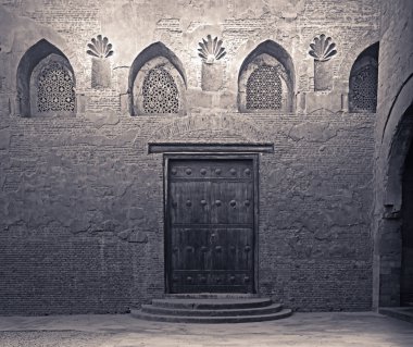 Aged wooden weathered door, perforated arched stucco window decorated with floral patterns, and three steps on stone bricks wall, Ibn Tulun Mosque, Cairo, Egypt clipart