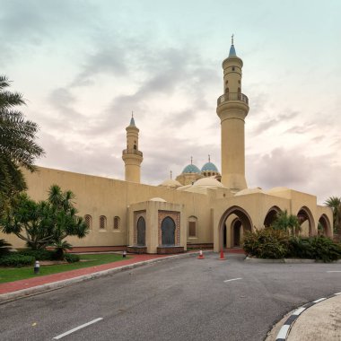 Ash Shaliheen Camii, Bandar Seri Begawan, Brunei Darussalam. Minareleri, kubbeleri ve kemerli girişleri olan, bulutlu bir gökyüzünün altında palmiye ağaçları ile çevrili İslami mimari