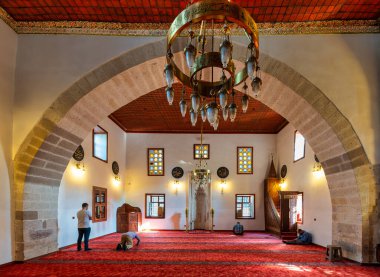 Konya, Türkiye - 6 Haziran 2025: Shems-i Tebrizi Camii ve Mezar İçi. Kırmızı halıda ibadet edenler, süslü avizeler, kemerler ve vitray pencereler.