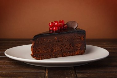 Çikolatalı pasta tabağı. Dekorasyon taze kırmızı kuş üzümü çilek, nane ve çikolata parçaları. Ahşap bir masa üzerinde bir tepside kek.