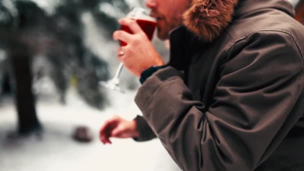 Homem bebendo cerveja de um copo com uma floresta embaçada e nevada como pano de fundo — Vídeo de Stock