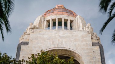 Devrim Anıtı 'nın Önü Ağaçlarla çevrili ve Bulutlu Gökyüzünün Altında