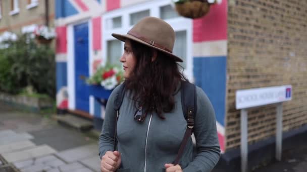 FHD女人，帽子在房子前面等着，房子漆成了英国国旗 — 图库视频影像