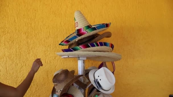 Vídeo de una mujer recogiendo un sombrero de pilas de sombreros mexicanos tradicionales — Vídeos de Stock