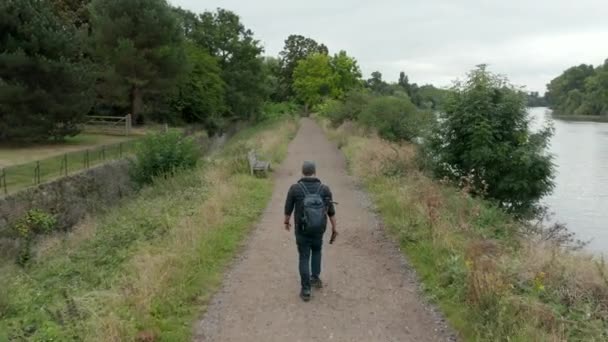 4k Aerial View of Man Walking on Trail Next to a River While He Switches His Cap — Stock Video